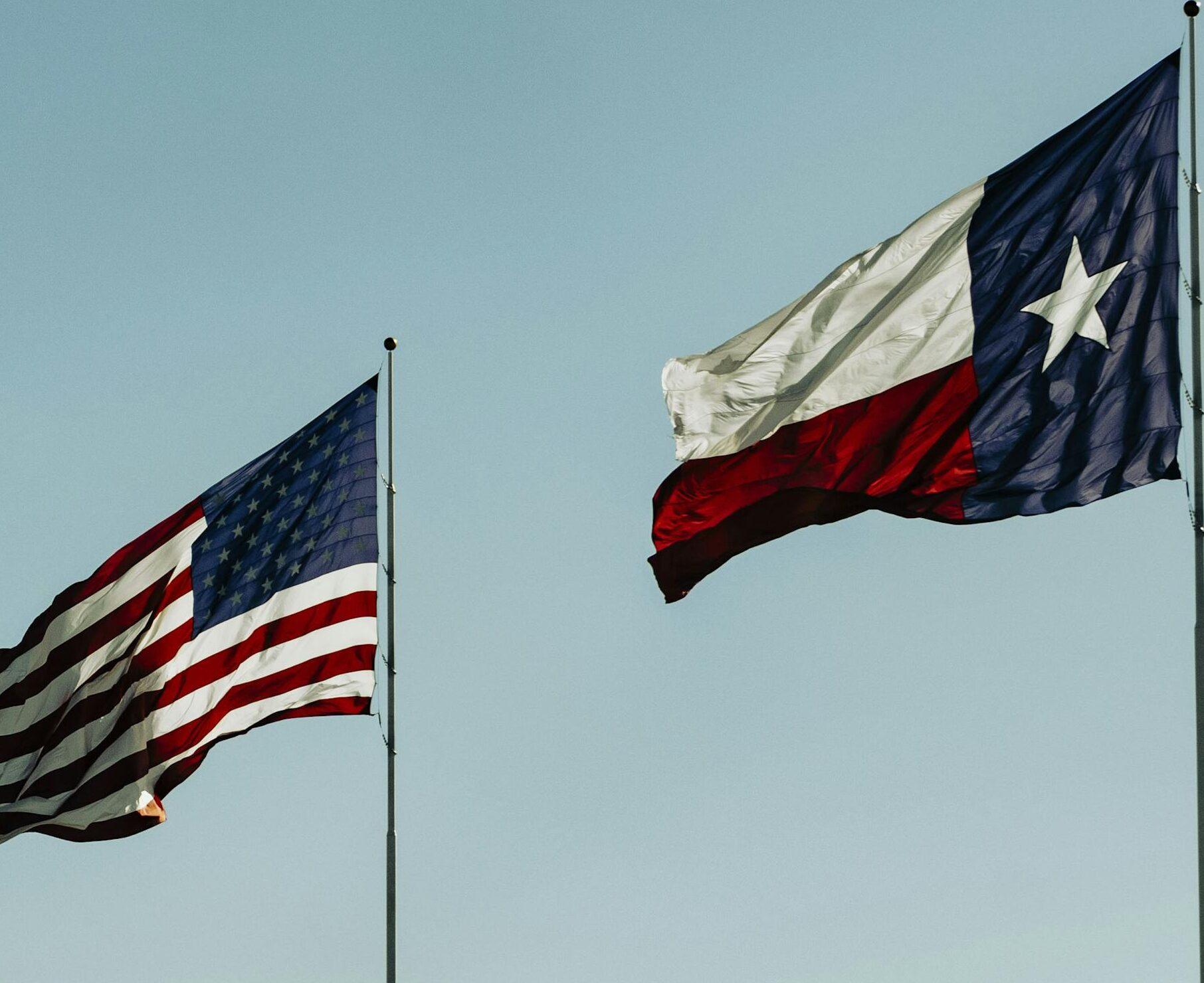 American and Texas flags waving under a clear blue sky, symbolizing patriotism and freedom.